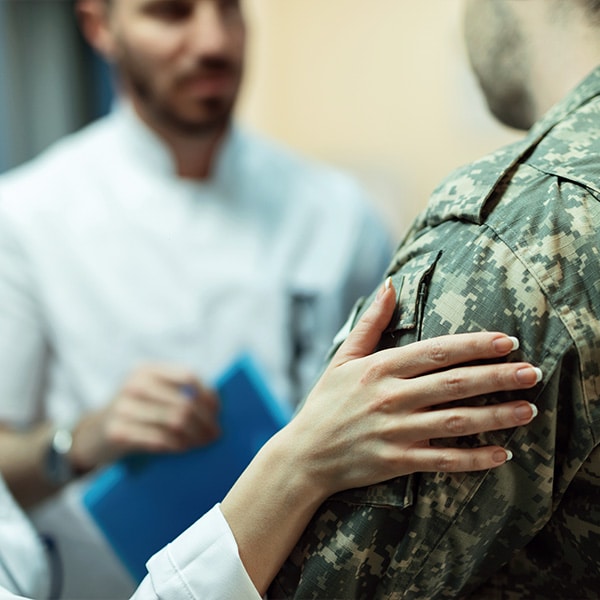 A medical professional's hand resting on a military professional's shoulder